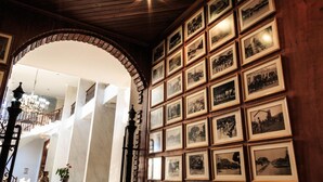Een statige zaal met een hoog plafond, een brede gewelfde doorgang en een wand versierd met zwart-wit foto's in lijsten.