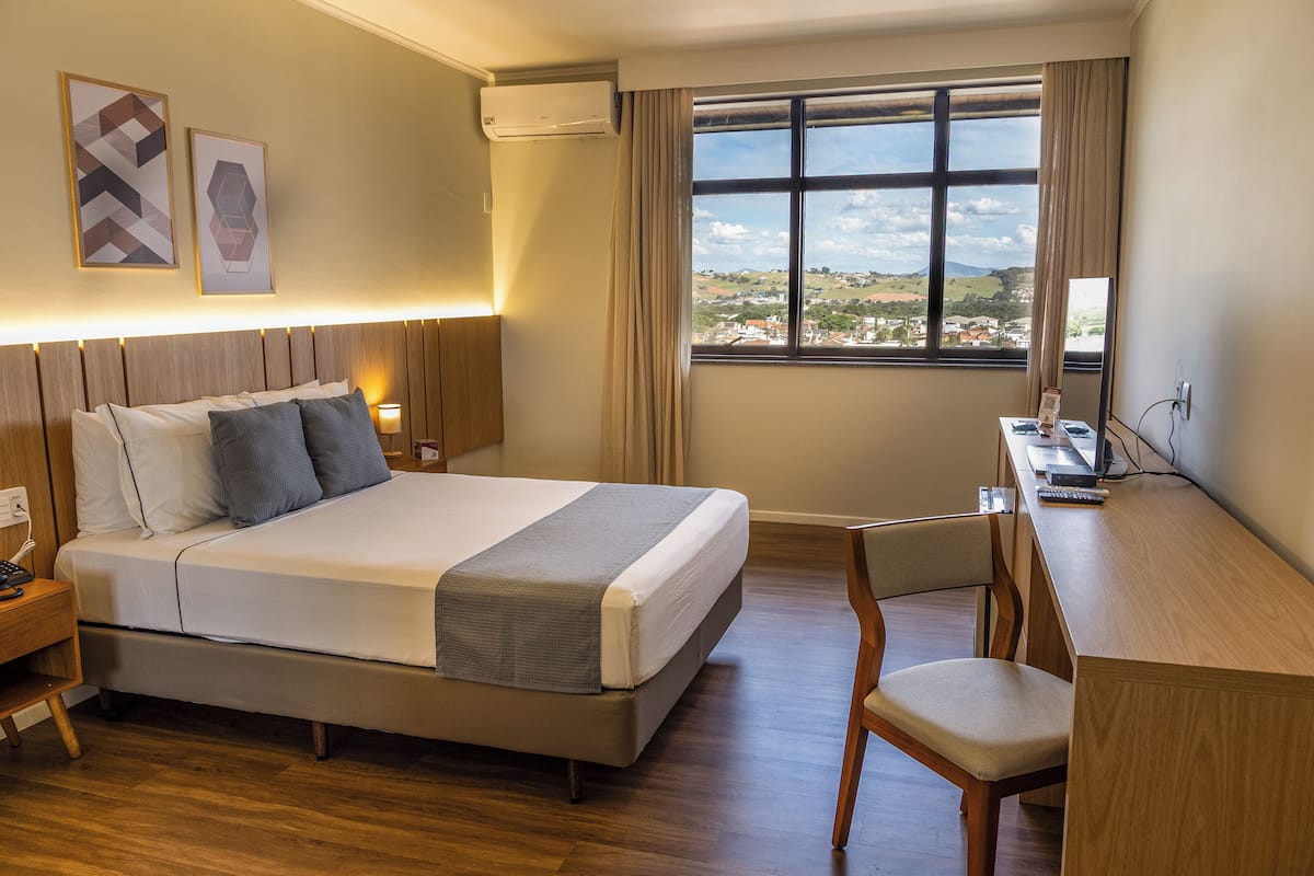 Ein Hotelzimmer mit Bett, Schreibtisch, Stuhl und Blick auf die Landschaft.