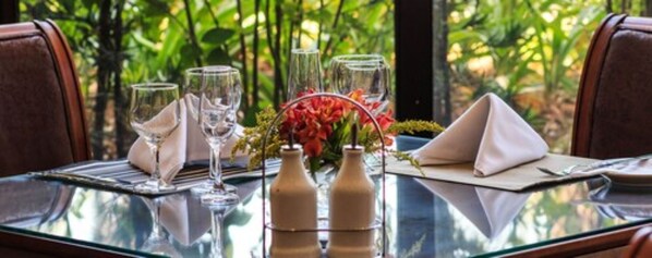 A dining table set with glasses, a vase of flowers, and a bottle. - Marques Plaza Hotel (Pouso Alegre)