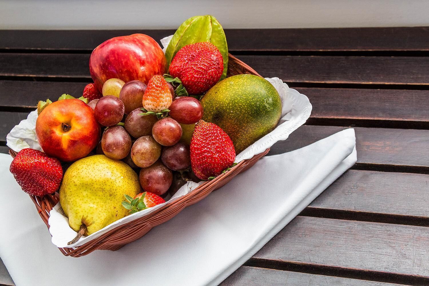 Een rieten mand vol verschillende soorten fruit op een houten bank.