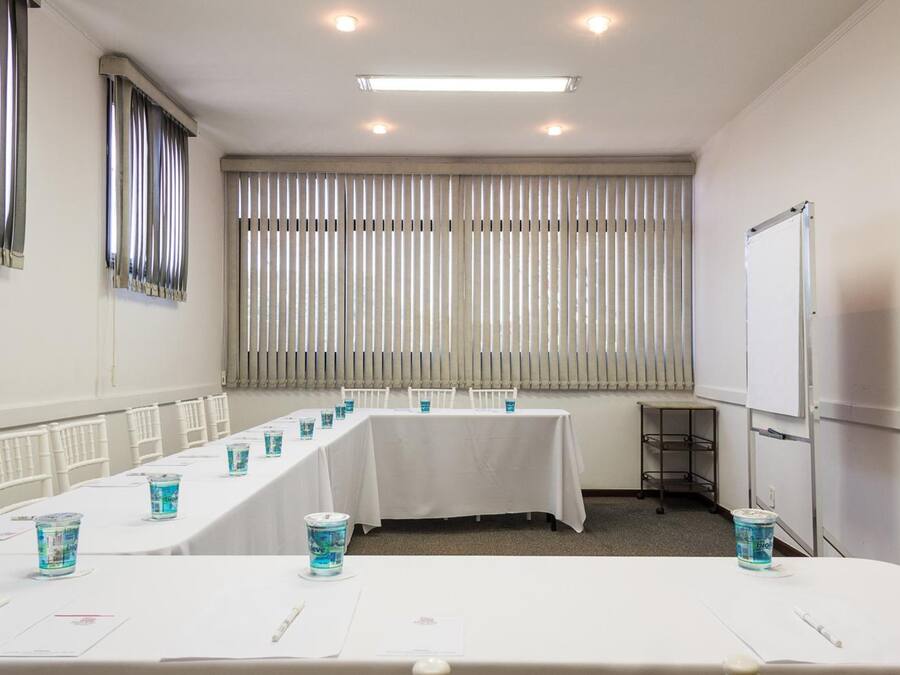 A conference room with a long table, chairs, a projector screen, and blinds on the windows.
