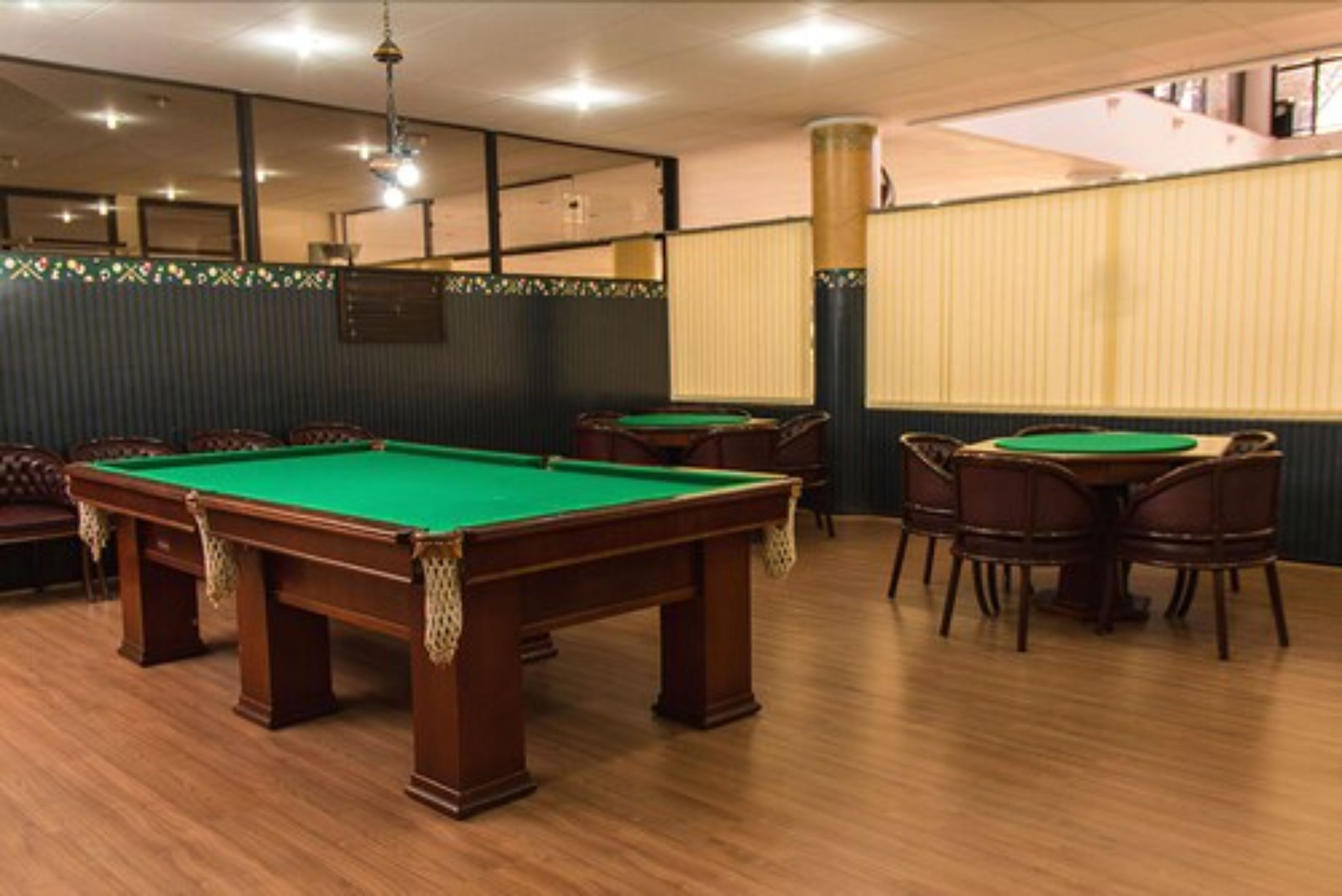 A billiards room with multiple pool tables, wooden flooring, and a high ceiling with recessed lighting.