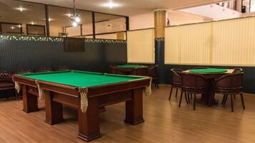 A billiards room with multiple pool tables, wooden flooring, and a high ceiling with recessed lighting.