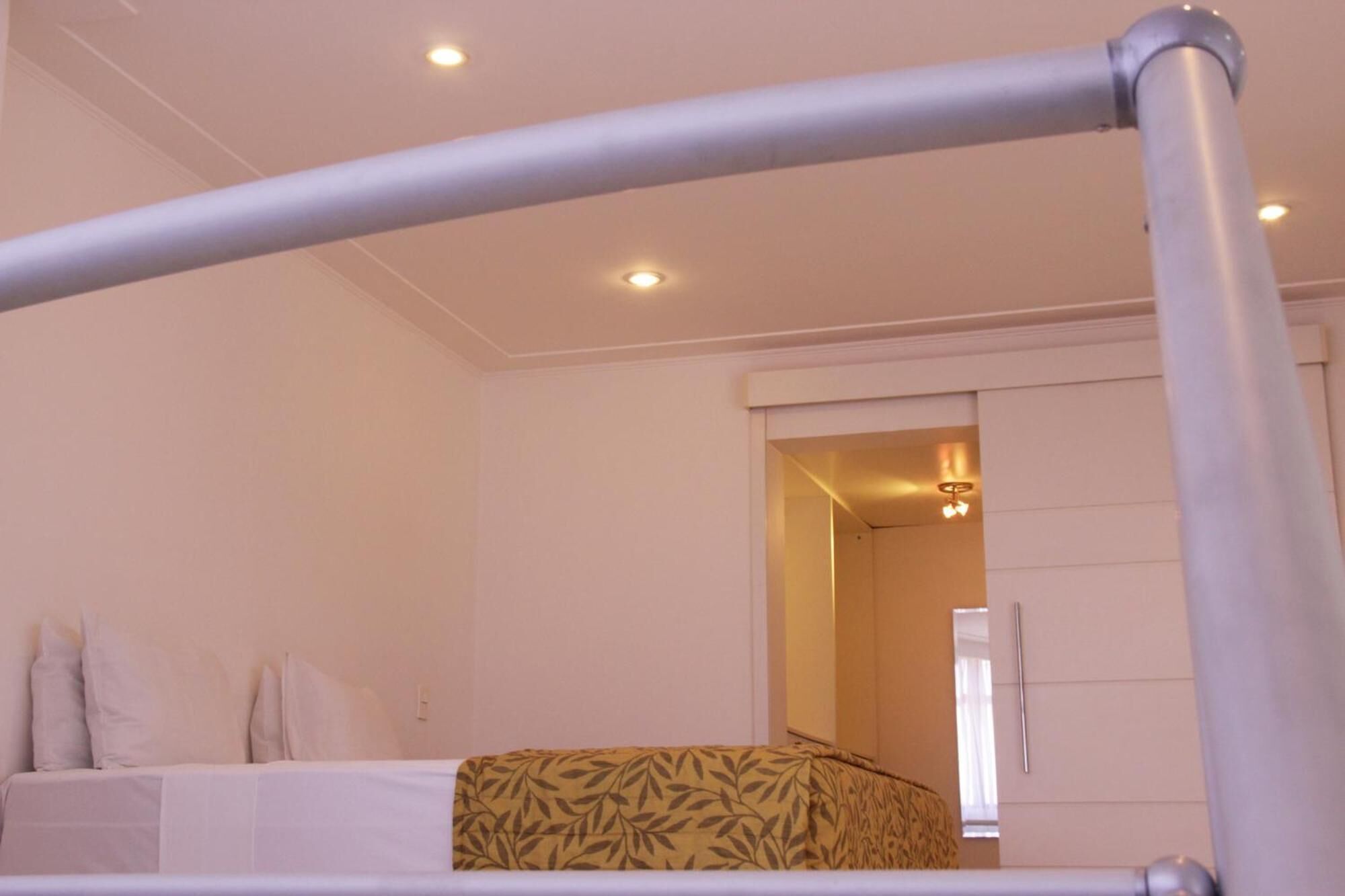Quarto de hotel com cama, manta estampada e teto com iluminação embutida.