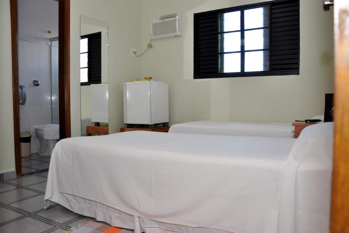 A hotel room with two beds, a white wardrobe, a mirror, and a window with blinds.