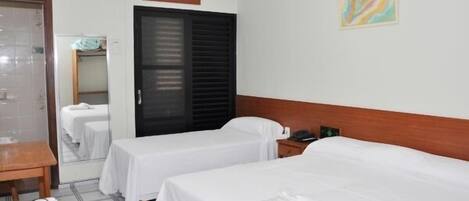 Una habitación de hotel con dos camas individuales, cabecero de madera, mesita de noche con teléfono y un espejo.