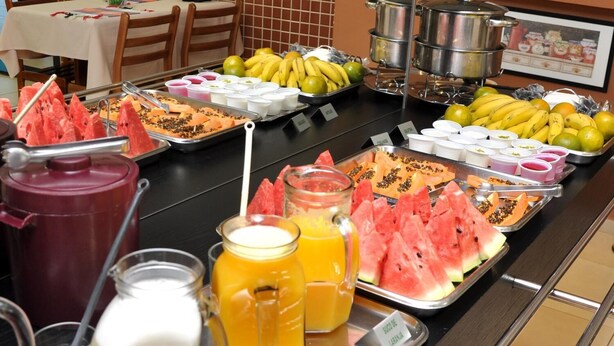 A buffet with various fruits, juices, and a pot of soup.