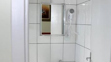 Un baño pequeño y limpio con azulejos blancos, un lavamanos, un espejo y un secador de pelo.