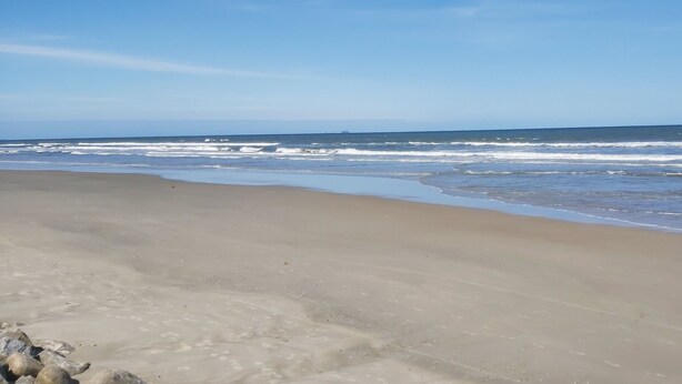 A beach with a wide sandy shore and gentle waves. - Pousada Girassol (Matinhos)