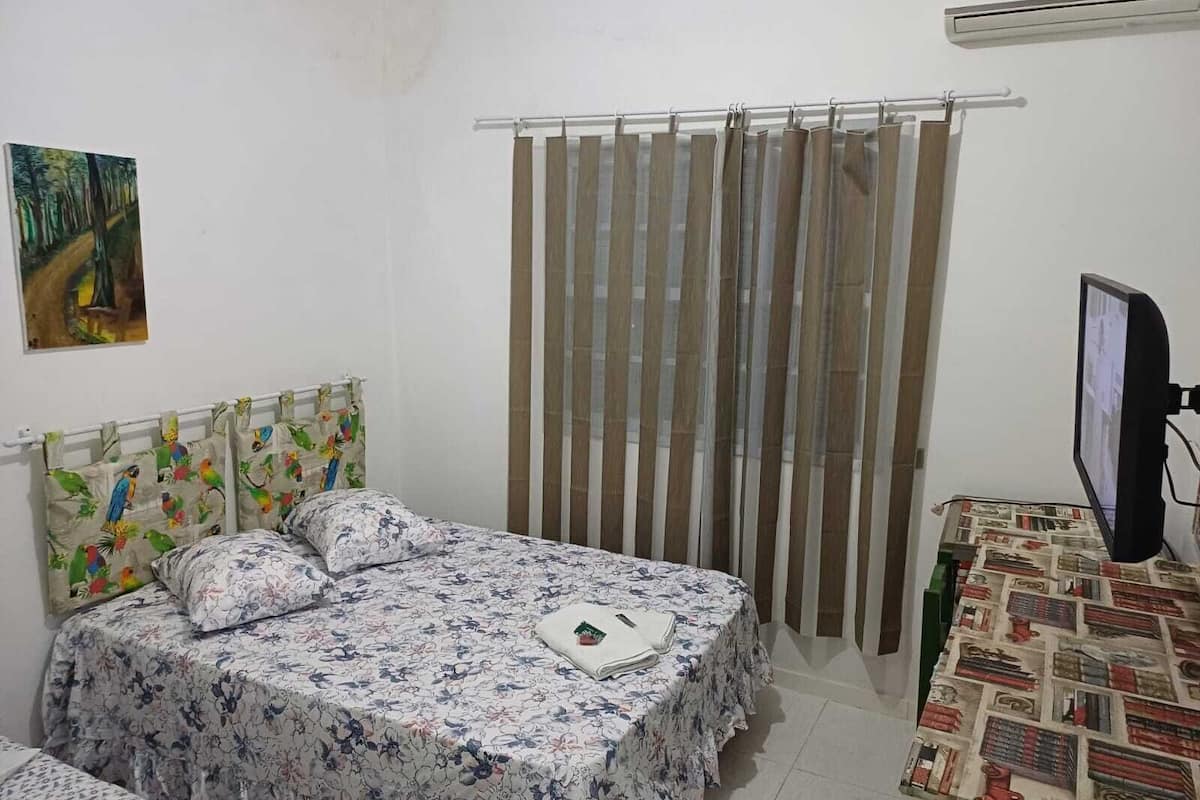 A bedroom with a bed, a curtain, a television, and a painting on the wall.