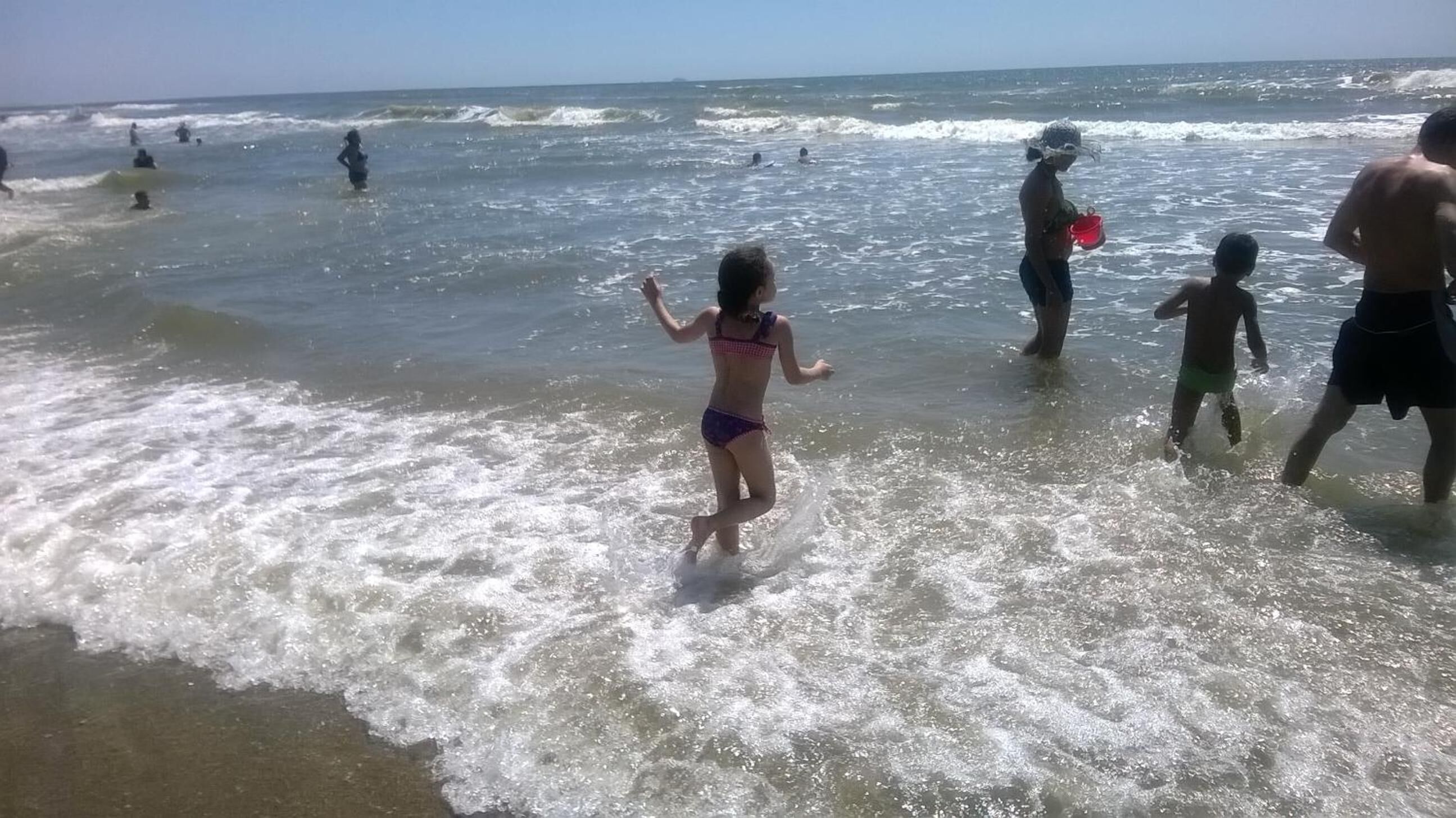 Une scène de plage avec des personnes dans l’eau et sur le rivage.