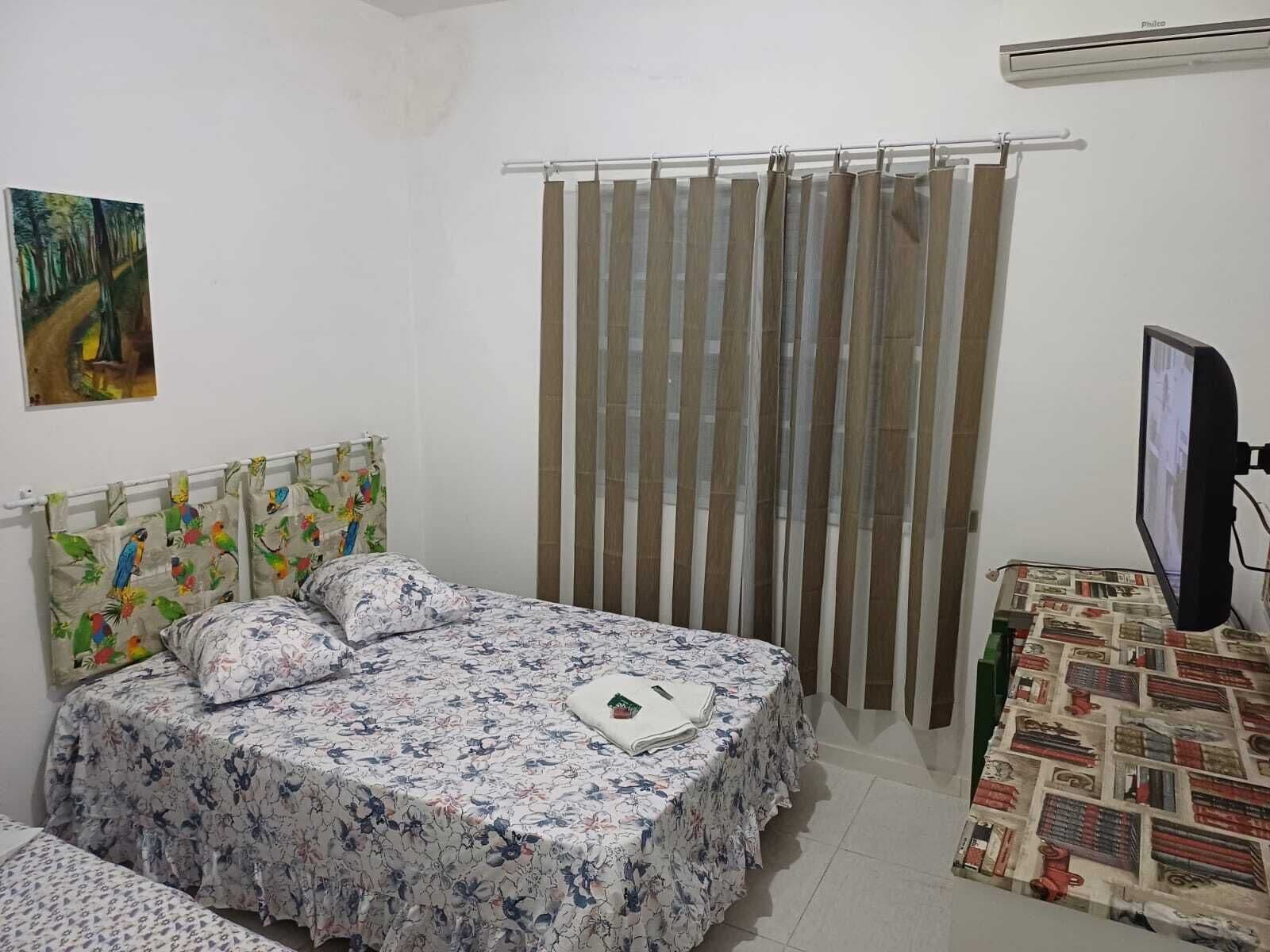 A bedroom with a bed, a curtain, a television, and a painting on the wall.