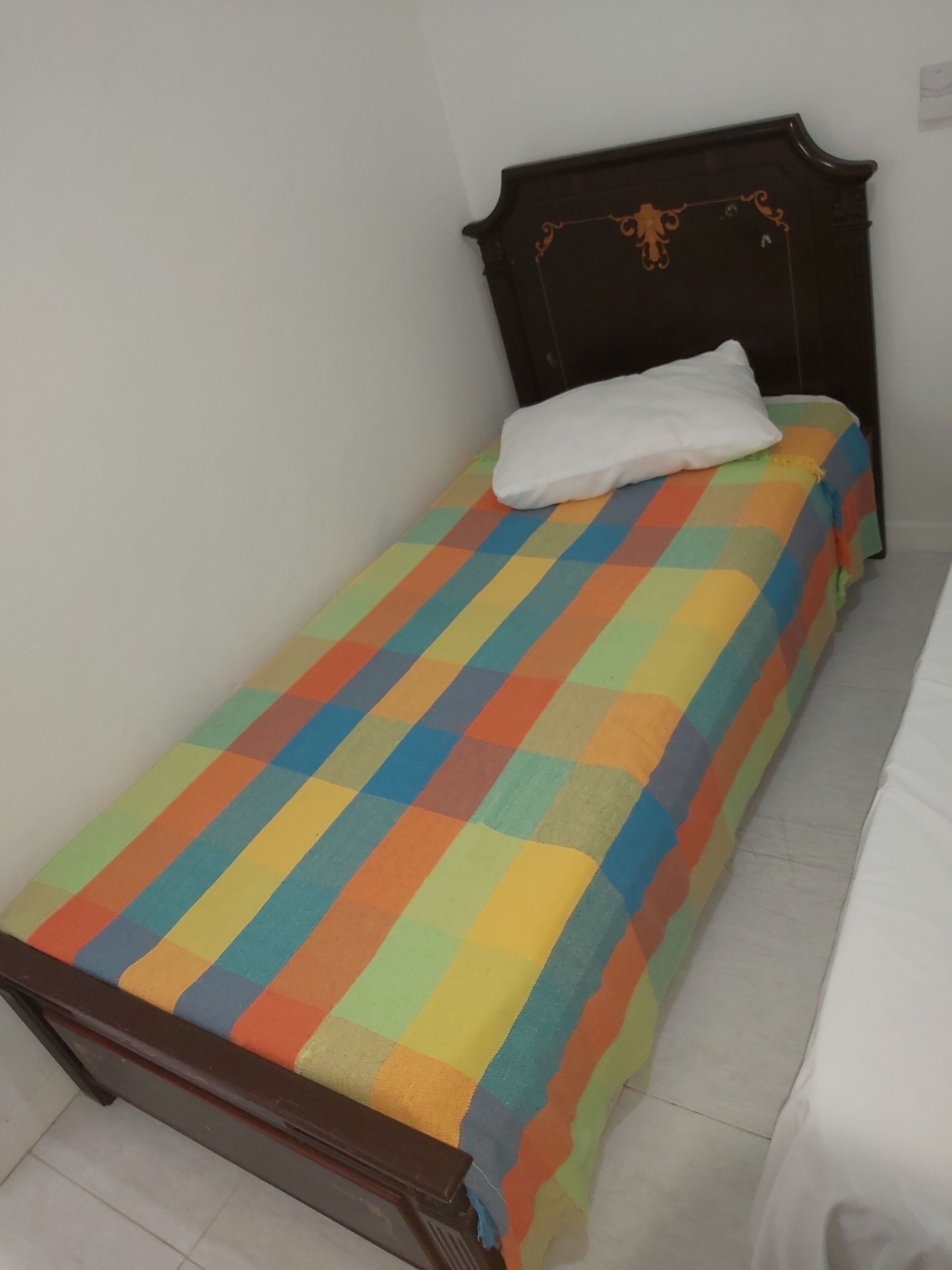 A small, single-bed room with a colorful checkered bedspread and a white pillow.