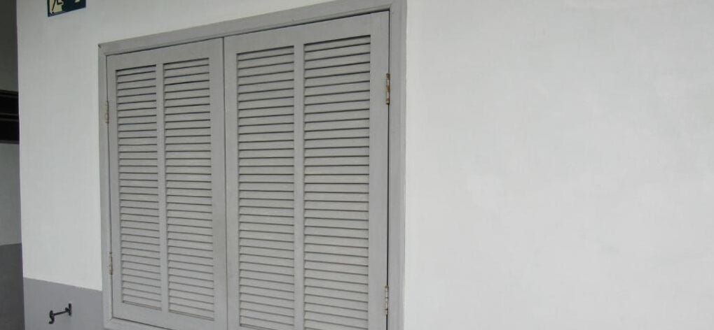A white wall with a large, closed, louvered door.