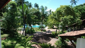 A lush garden with a pool, palm trees, and a wooden deck. - Hotel 7 Colinas (Olinda)