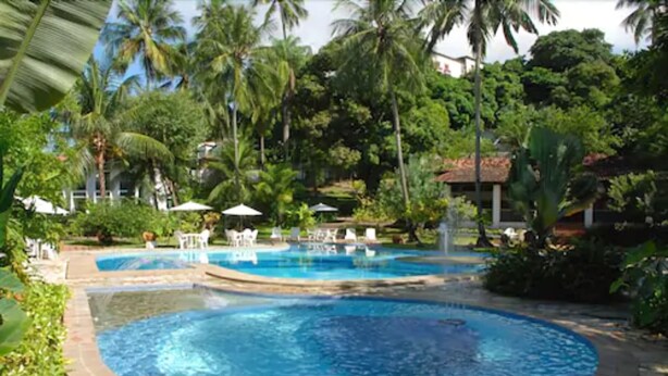 A pool area with two circular pools, surrounded by palm trees and greenery. - Hotel 7 Colinas (Olinda)
