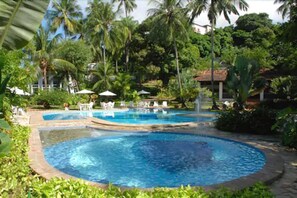 Un área de piscina con dos piscinas circulares, rodeada de palmeras y vegetación.