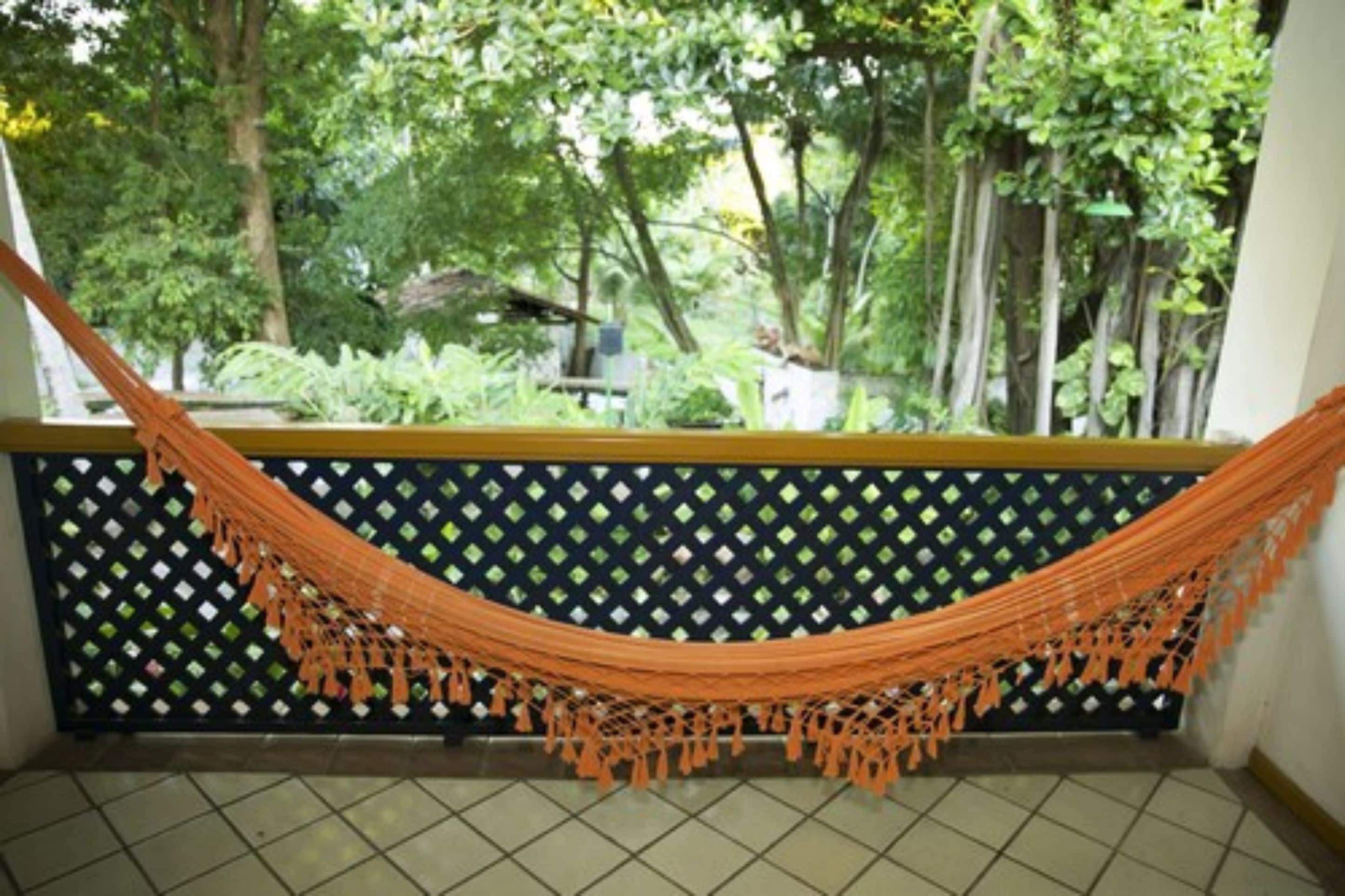 A hammock hanging between a lattice wall and a tiled floor, with a view of lush greenery outside.