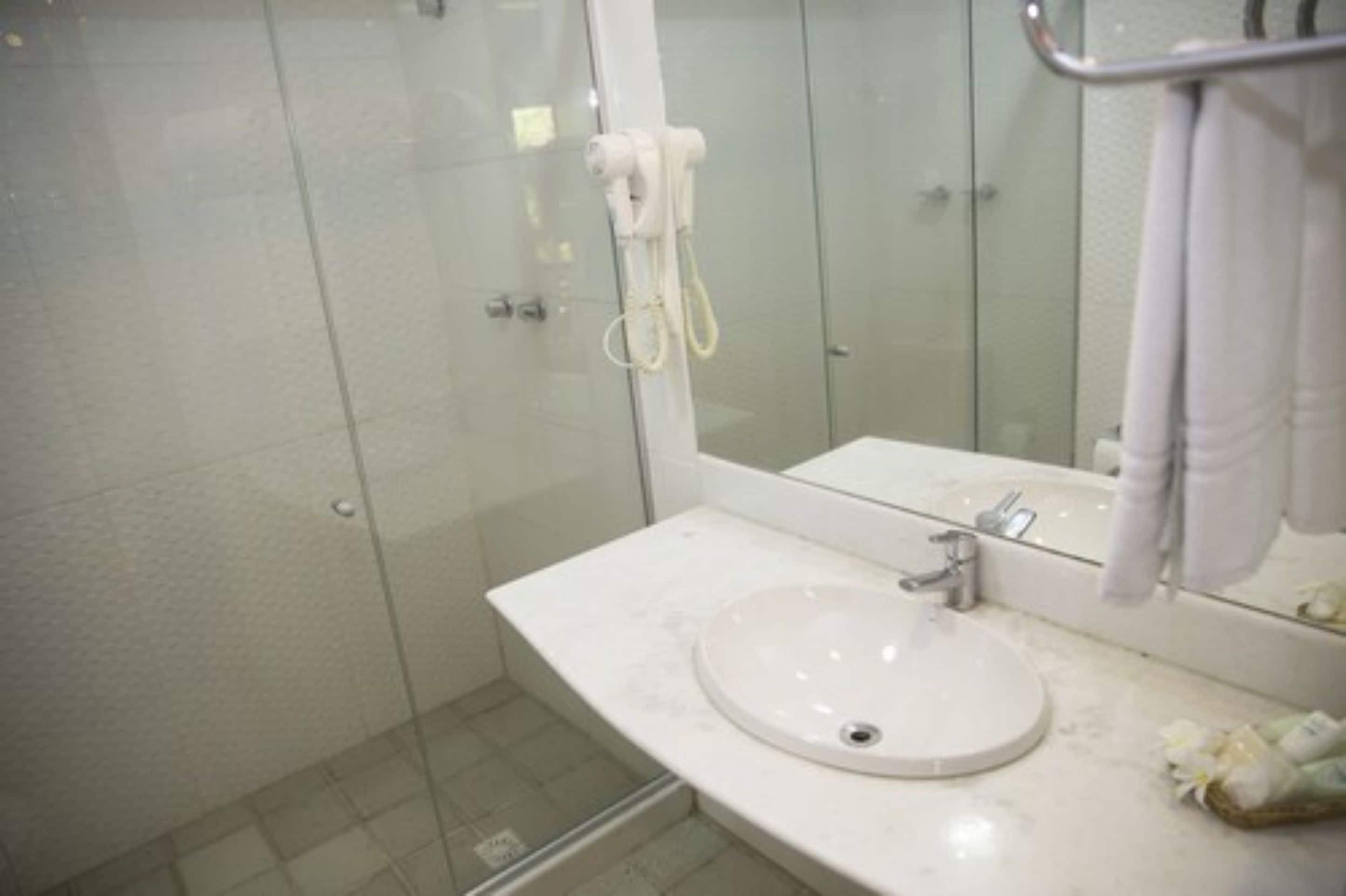 Ein Badezimmer mit Duschkabine aus Glas, einem weißen Waschbecken und einem Spiegel mit Handtuchhalter.