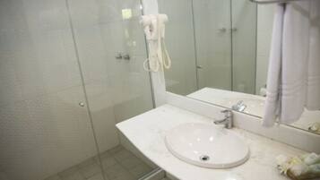 Ein Badezimmer mit Duschkabine aus Glas, einem weißen Waschbecken und einem Spiegel mit Handtuchhalter.