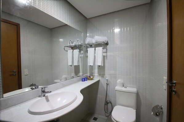 Et badeværelse med en hvid vask, toilet og et glasstativ til håndklæder.