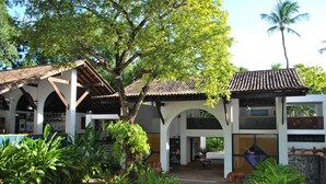A courtyard with a tiled floor, surrounded by plants and trees, and a building with a tiled roof and white walls. - Hotel 7 Colinas (Olinda)