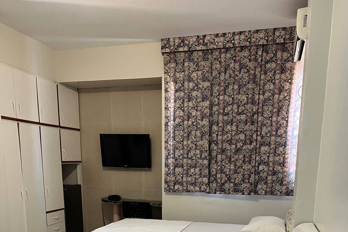 Ein Hotelzimmer mit zwei Betten, einem Fernseher, einem Kleiderschrank und einem Fenster mit floralem Vorhang.