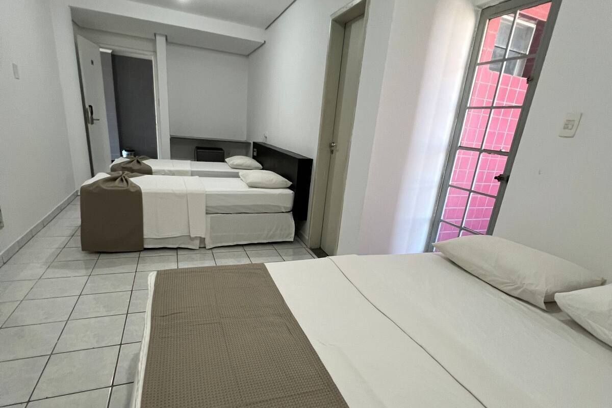 Ein Hotelzimmer mit zwei Betten, einem großen Fenster mit rosa Jalousien und einem Fliesenboden.