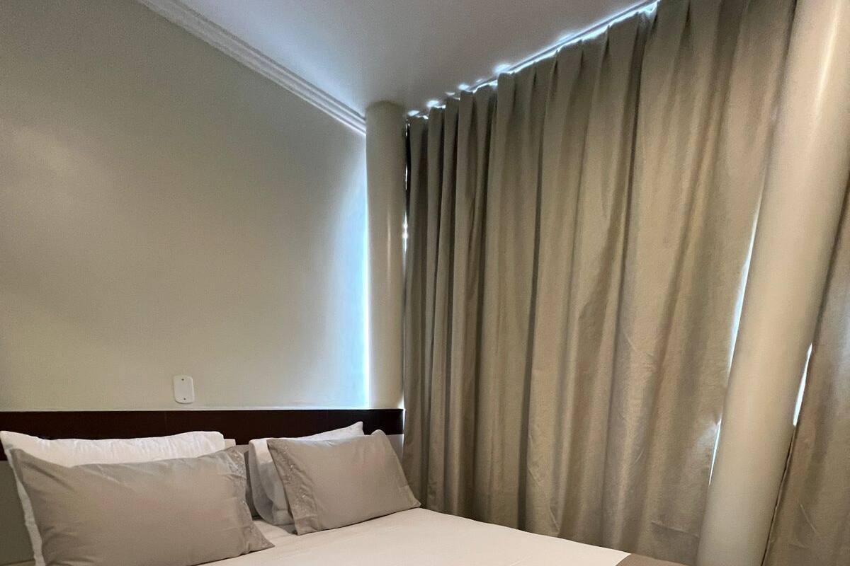 Ein Hotelzimmer mit einem großen Bett, beigen Vorhängen und einem ordentlich bezogenen Bett mit einer braunen Decke.