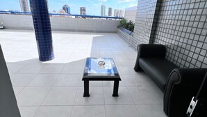 Une terrasse sur le toit avec une table à plateau en verre, un canapé en cuir noir et un tapis bleu orné d’un logo.