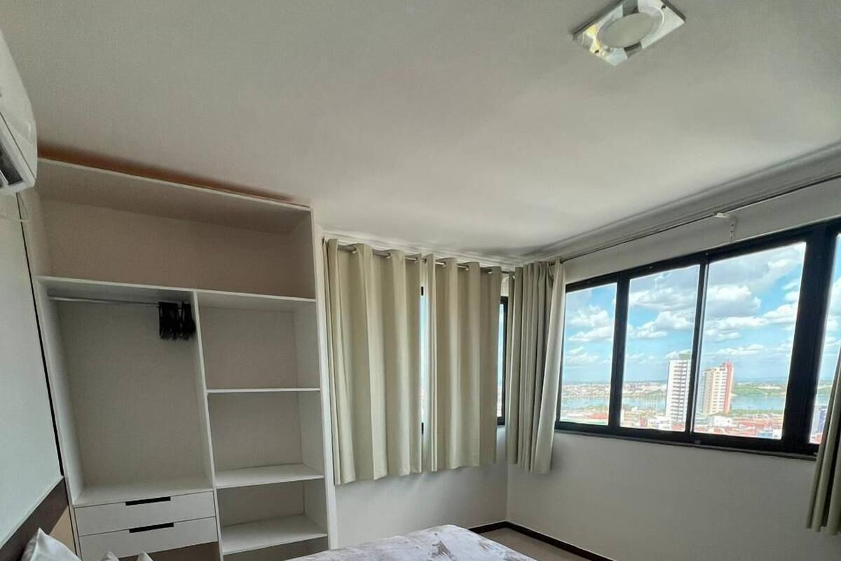 Ein Schlafzimmer mit einem Bett, einem Kleiderschrank, einem Fenster mit Blick auf die Stadt und einer Deckenleuchte.