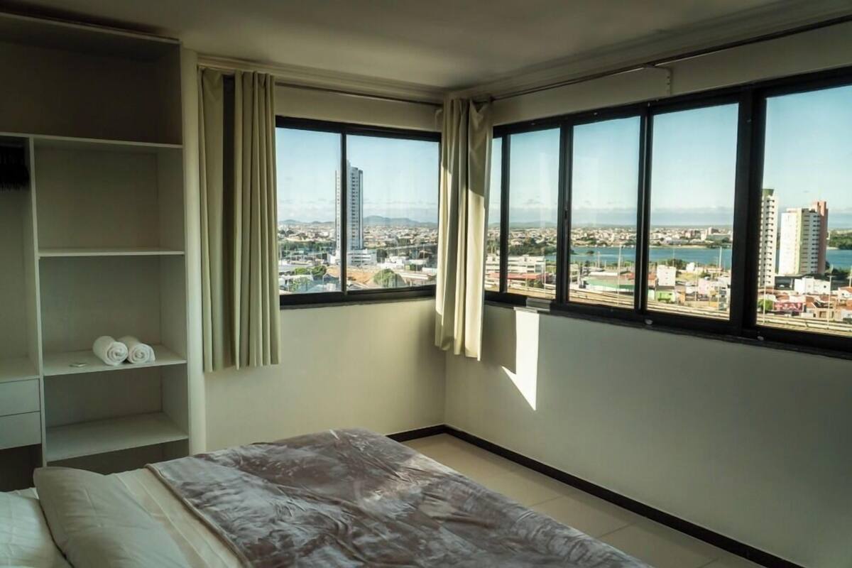 Ein Hotelzimmer mit großem Fenster und Blick auf die Stadt, einem Bett mit Decke und einem Regal mit Handtüchern.