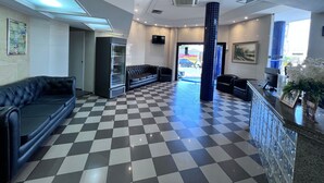 Un hall d’entrée avec un sol à carreaux, un canapé en cuir noir, une vitrine et un comptoir d’accueil.