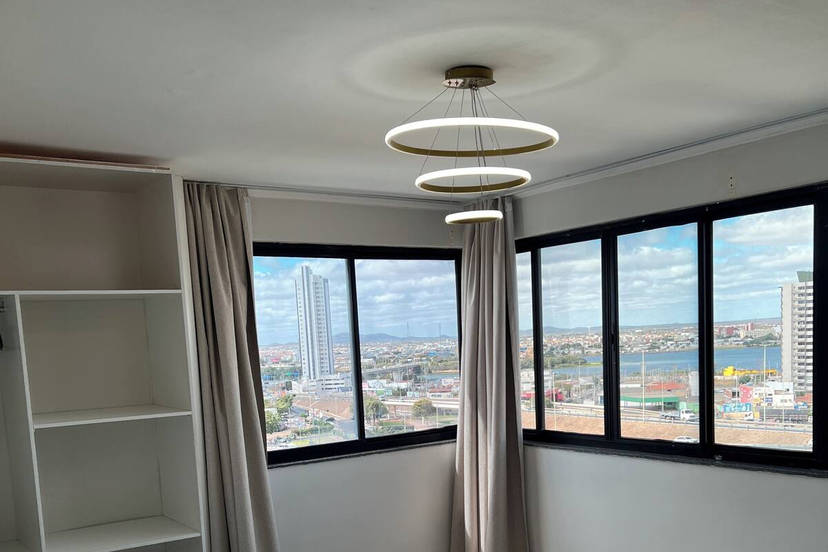 Ein Hotelzimmer mit Bett, Kleiderschrank und großen Fenstern mit Blick auf die Stadt.