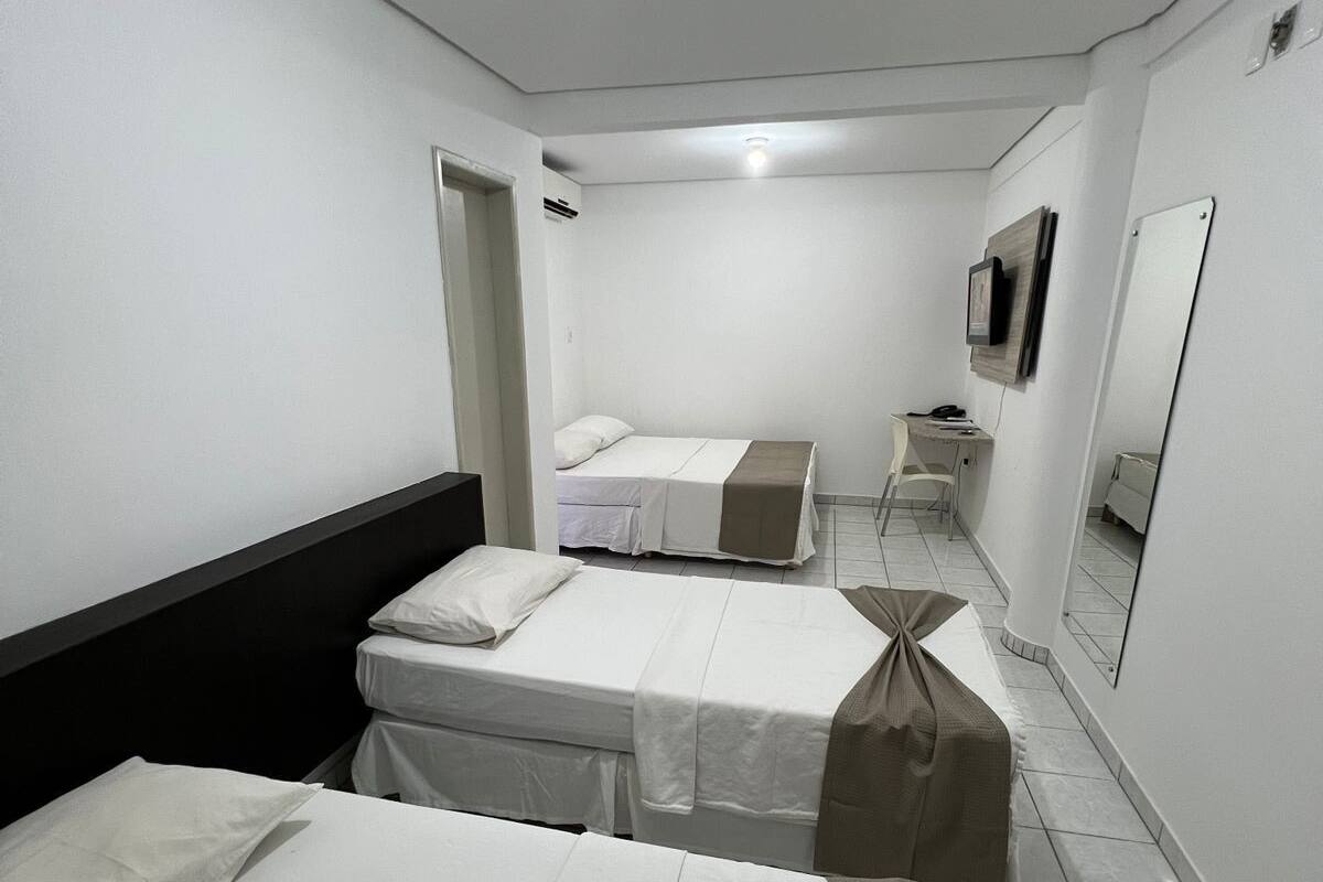 Ein Hotelzimmer mit zwei Betten, einem Schreibtisch, einem Stuhl, einem Spiegel und einem Fernseher.