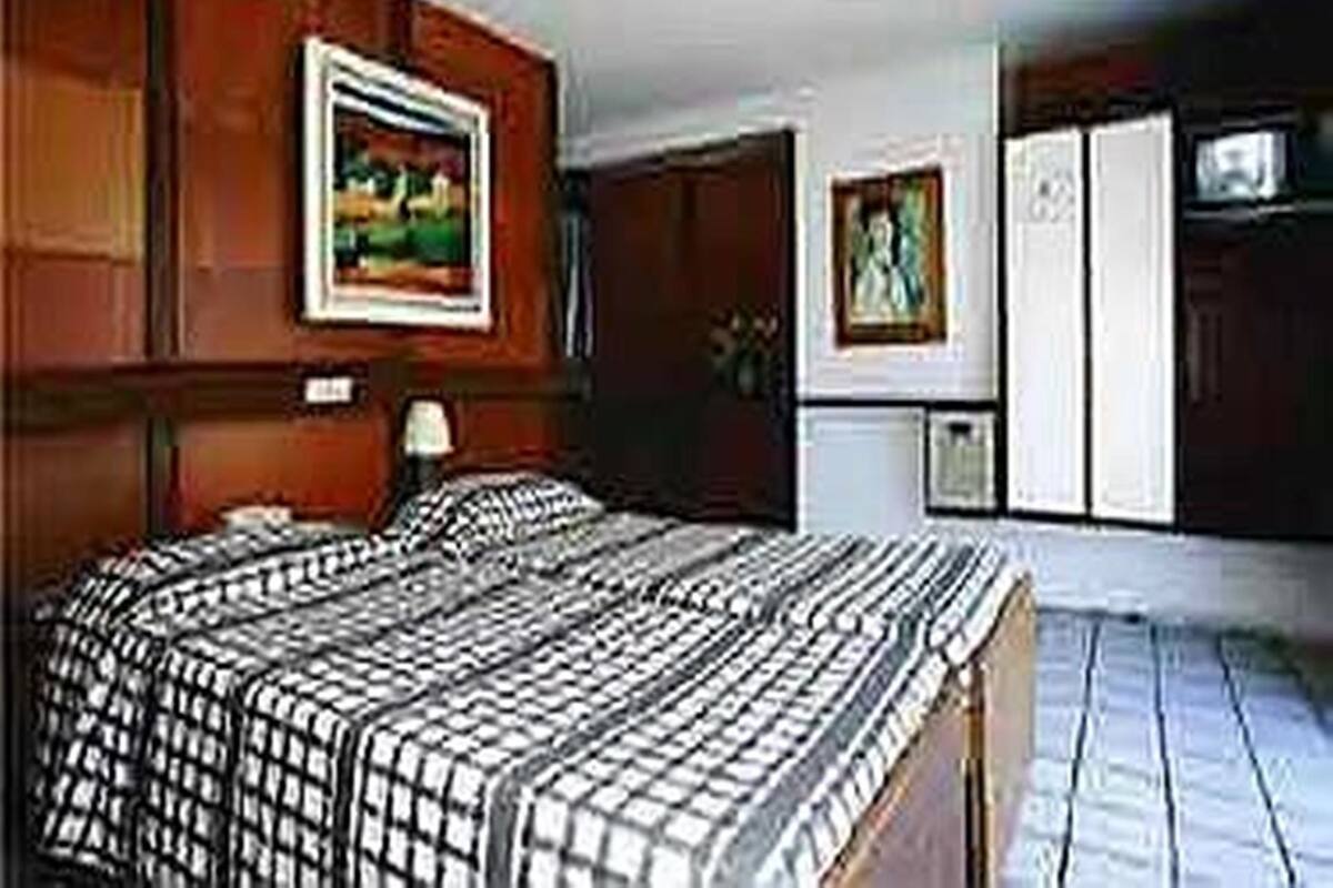 A hotel room with a large bed, wooden paneling on the walls, a painting above the bed, and a television on the right side.