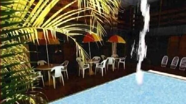 An indoor pool area with a waterfall feature, surrounded by tables and chairs, and palm trees. - Arcada Hotel E Bistrô (RECIFE)