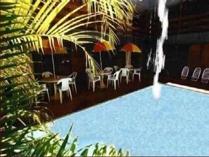 An indoor pool area with a waterfall feature, surrounded by tables and chairs, and palm trees. - Arcada Hotel E Bistrô (RECIFE)