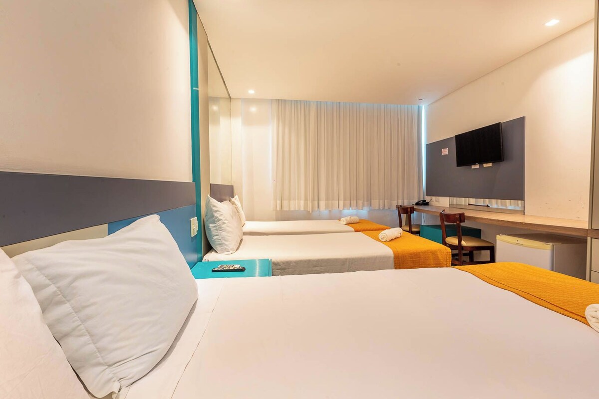 Una habitación de hotel con dos camas, un escritorio, una silla, un televisor y un ventanal con cortinas.