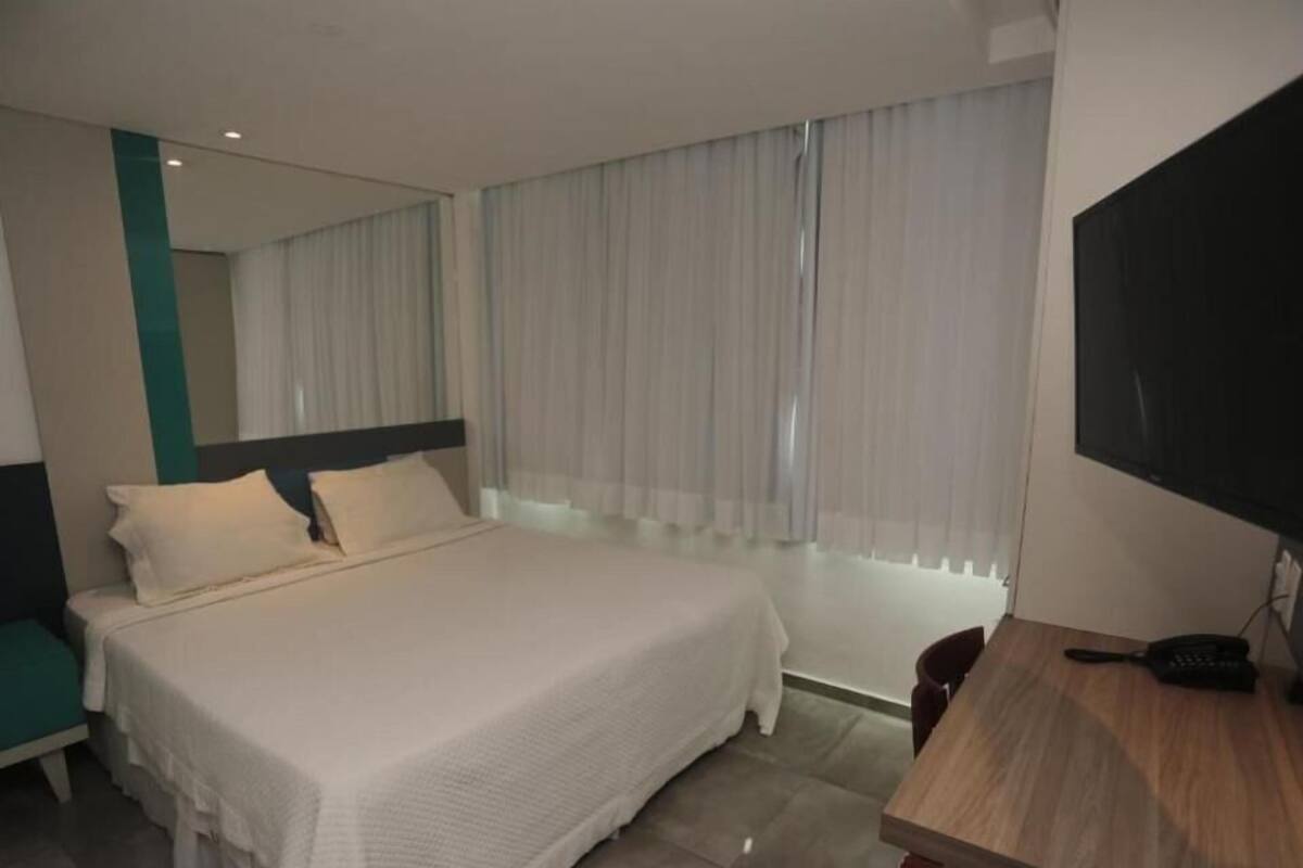 Ein Hotelzimmer mit Bett, Schreibtisch, Fernseher und einem Fenster mit Vorhängen.