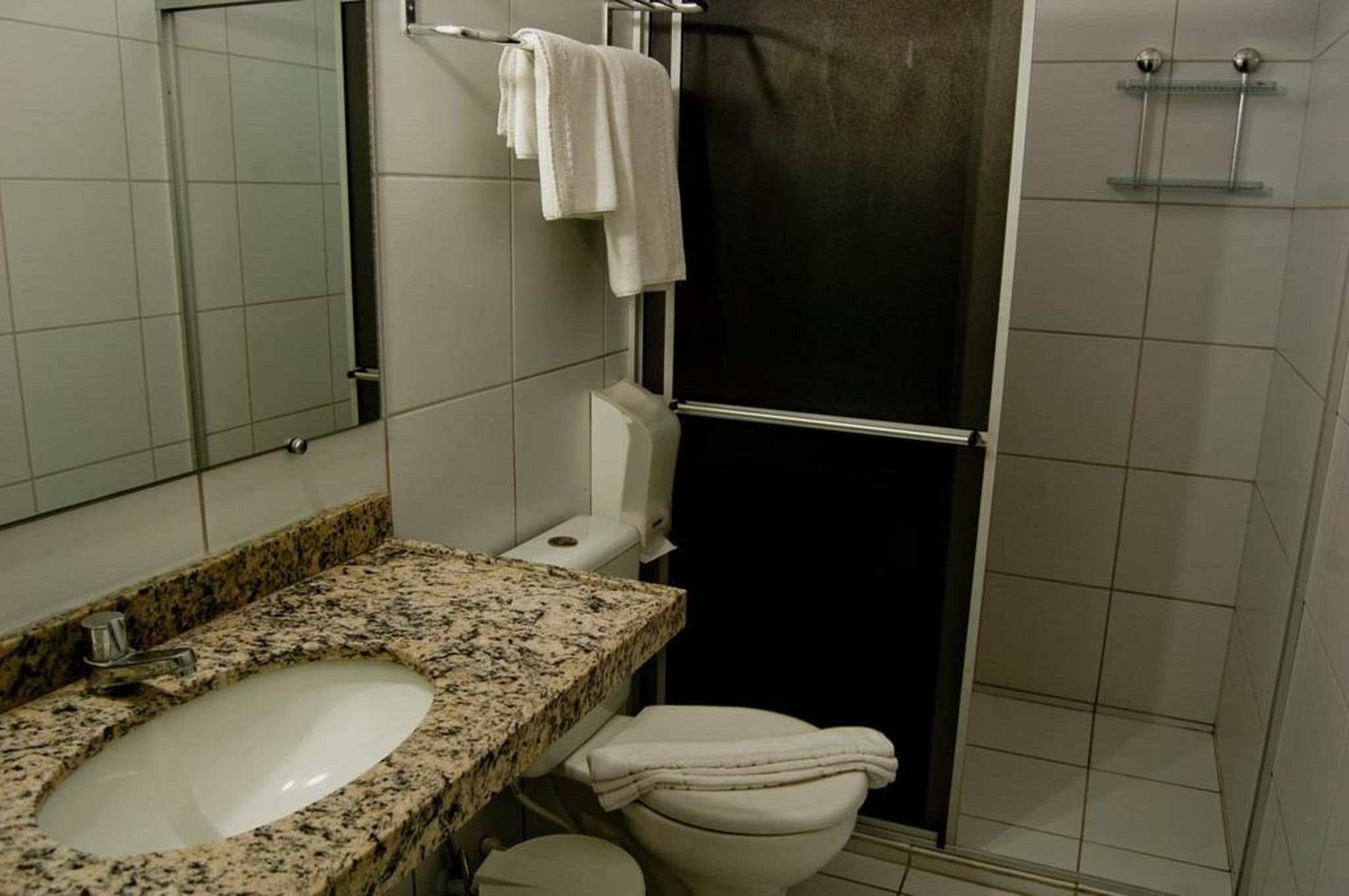 A bathroom with a granite countertop sink, a white toilet, a black shower enclosure, and a towel rack.