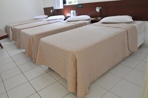 A hotel room with four single beds, each with a quilted bedspread, a bedside table, and a lamp. - Rede Andrade Navegantes (Recife)