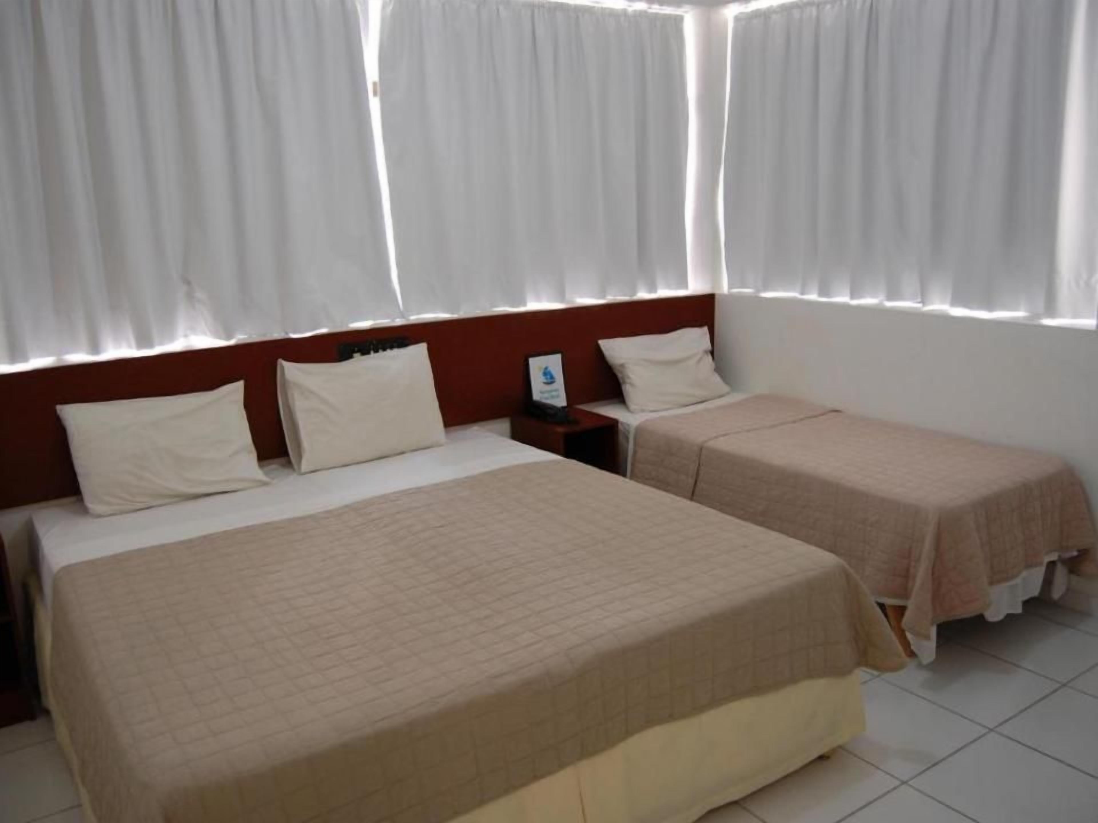 Quarto de hotel com duas camas, uma mesa de cabeceira e uma janela com cortinas.