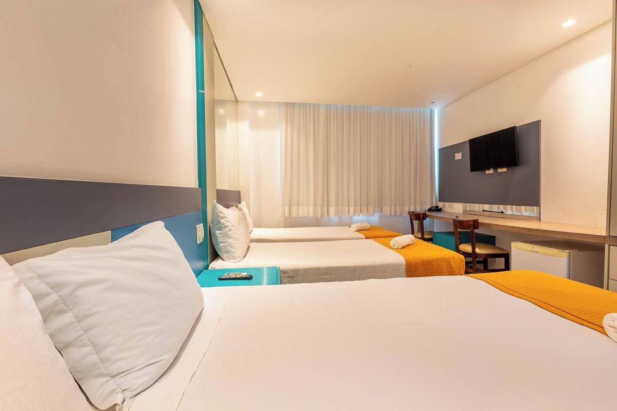 Ein Hotelzimmer mit zwei Betten, einem Schreibtisch, einem Fernseher und einem Fenster mit Vorhängen.