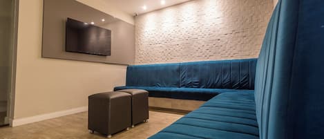 A modern living room with a sectional sofa, a flat-screen TV mounted on the wall, and a patterned wall.