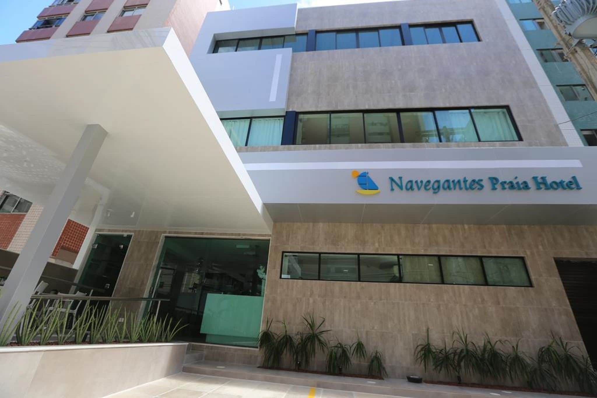 Um hotel moderno com fachada plana, janelas amplas e placa com o nome Navegantes Praia Hotel.