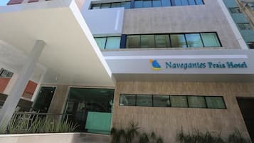 Um hotel moderno com fachada plana, janelas amplas e placa com o nome Navegantes Praia Hotel.