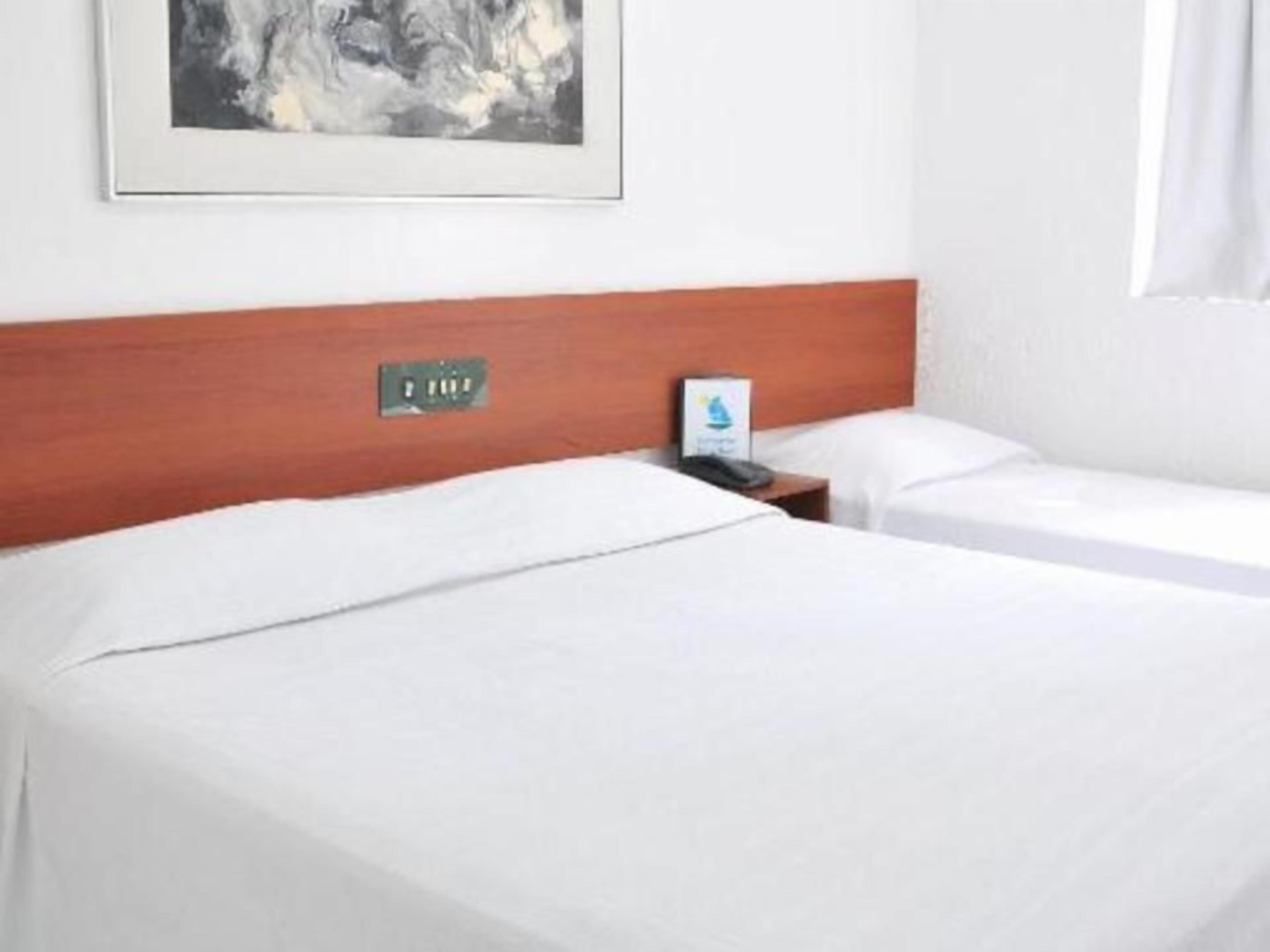 A hotel room with two beds, a wooden headboard, a framed artwork on the wall, and a bedside table with a lamp.