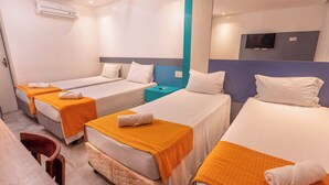 Ein Hotelzimmer mit drei Einzelbetten, jedes mit einer orangefarbenen Decke und einem weißen Kopfkissen. Es gibt einen kleinen Tisch mit einem Stuhl, einen Nachttisch und ein an der Wand befestigtes Fernsehgerät.