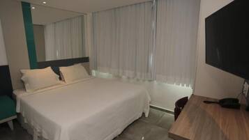 Una habitación de hotel con cama, escritorio, silla, televisor y ventana con cortinas.